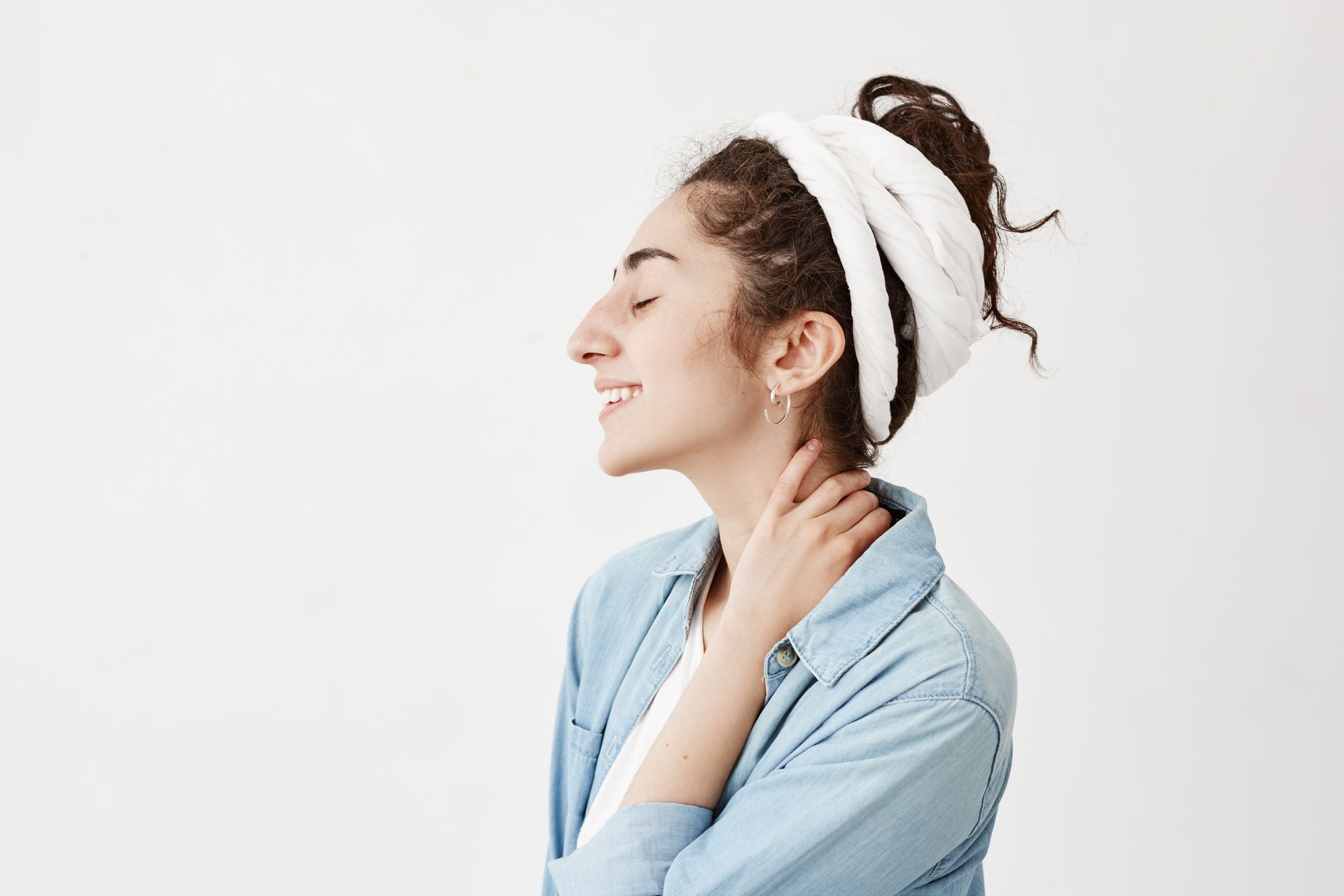 A woman with a towel around her head is smiling and holding her neck.