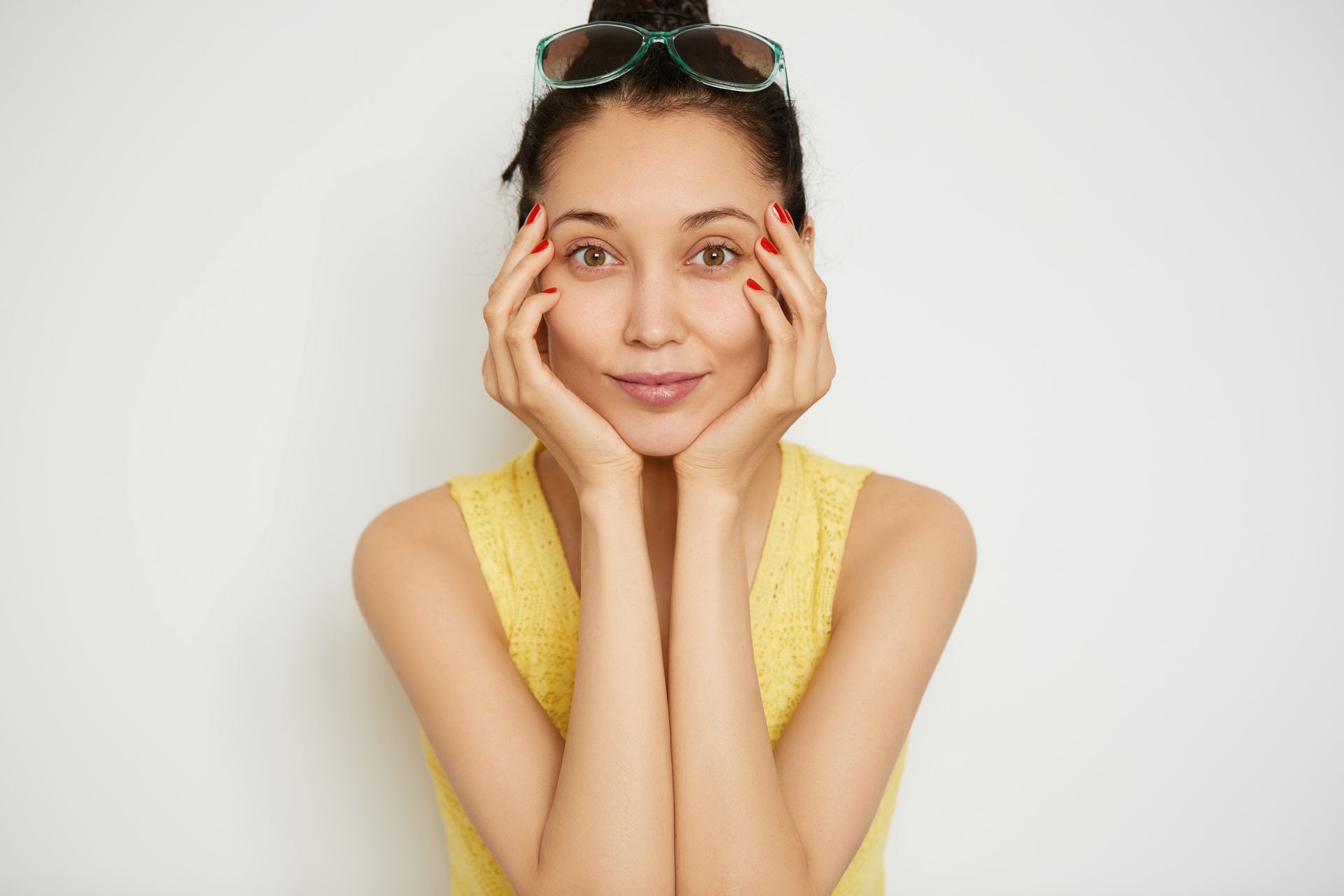 A woman wearing sunglasses and a yellow tank top is holding her face with her hands.