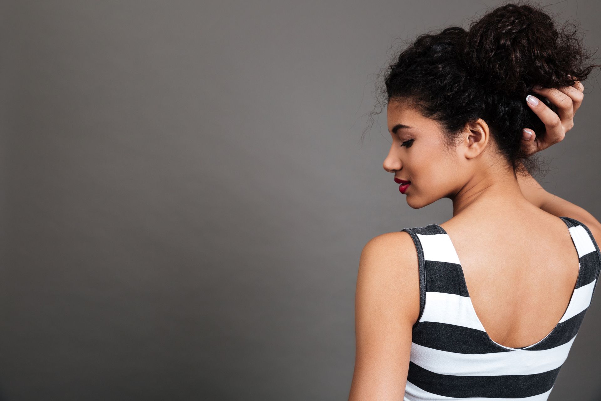 A woman in a striped tank top is holding her hair in a bun.