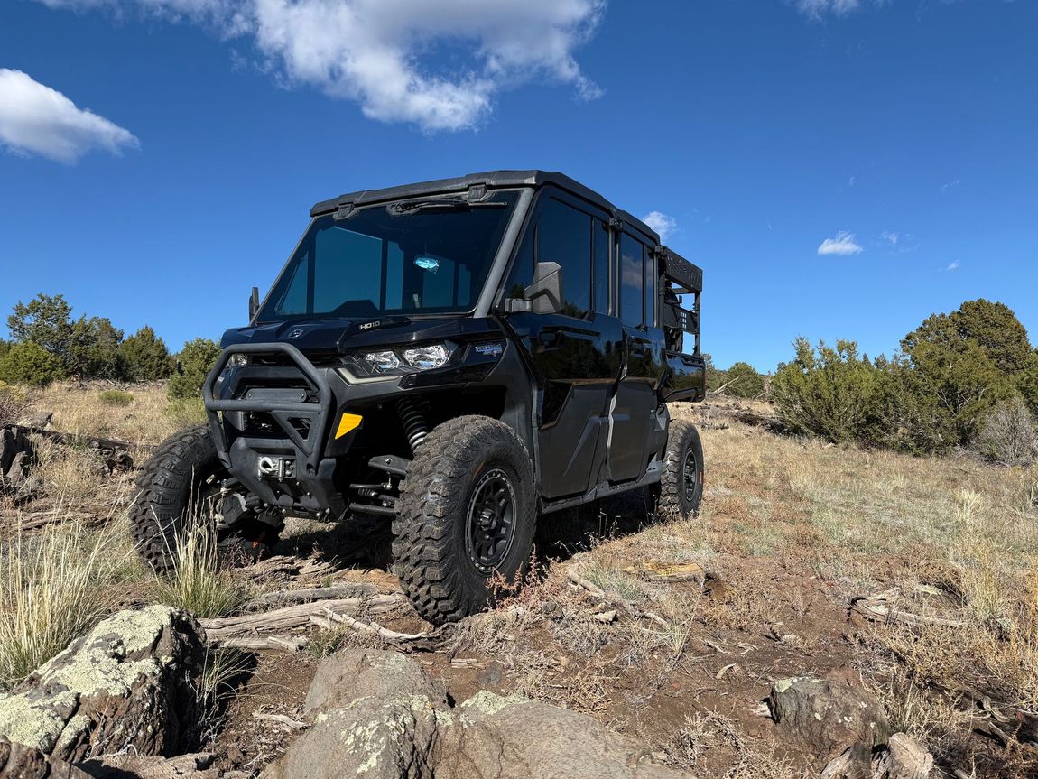 Black off-road vehicle on a rocky hillside under a blue sky, with trees in the background.