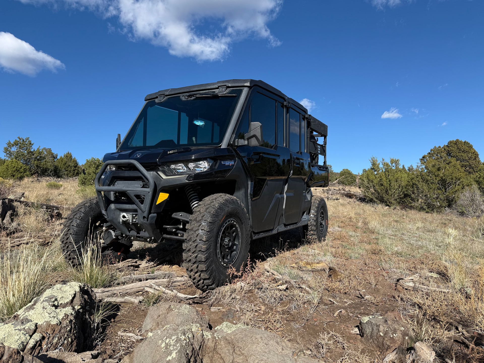 Black off-road vehicle on a rocky hillside under a blue sky, with trees in the background.