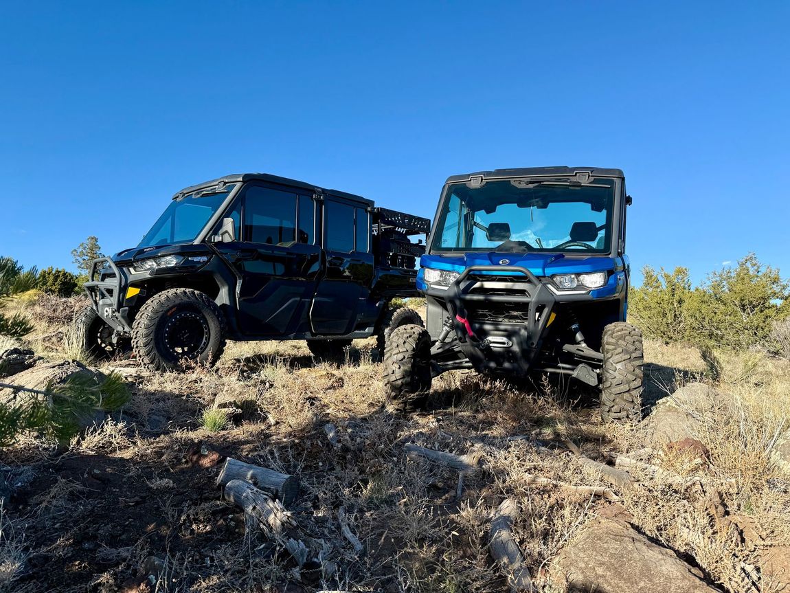Two off-road vehicles parked on a hillside under a blue sky; one black, one blue.
