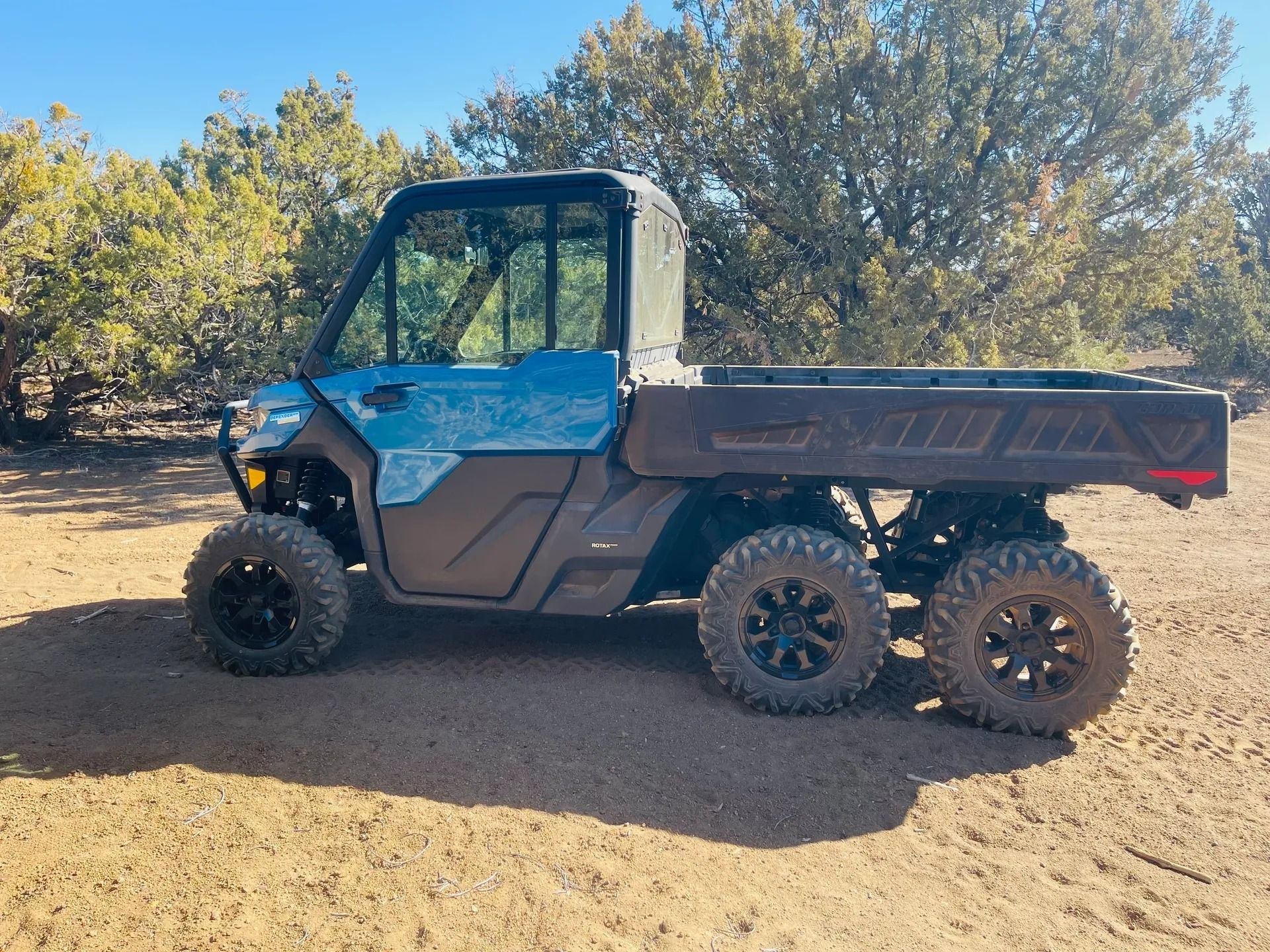 Blue and black 6-wheeled UTV with a dump bed on a dirt path, surrounded by trees.