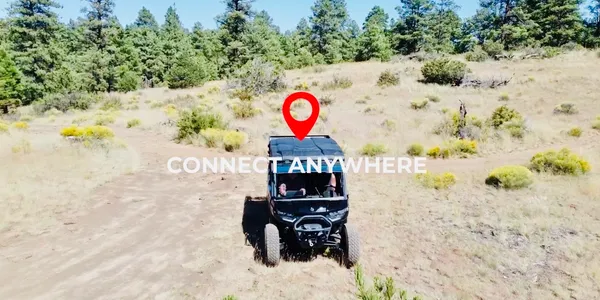 A black ATV on a dirt path in a hilly, grassy landscape. A location pin is above the ATV; text reads “CONNECT ANYWHERE”.