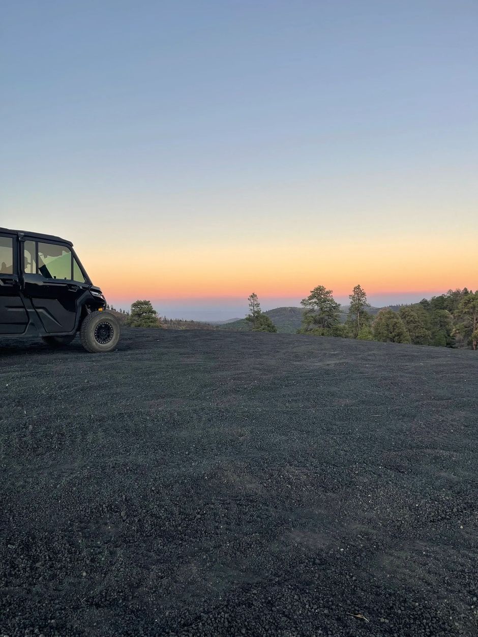 Black UTV on a gravel hill at sunset. Orange and blue sky over distant trees.
