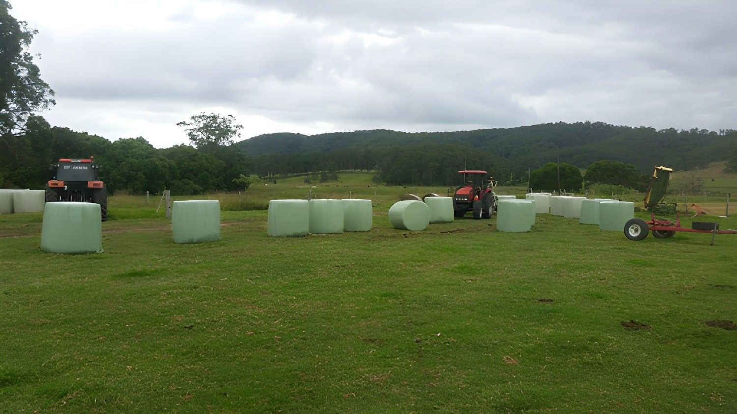 A Tractors Wrapping Hay Bales in A Green Field — Barry Brown Rural Contracting Service in Tinonee, NSW