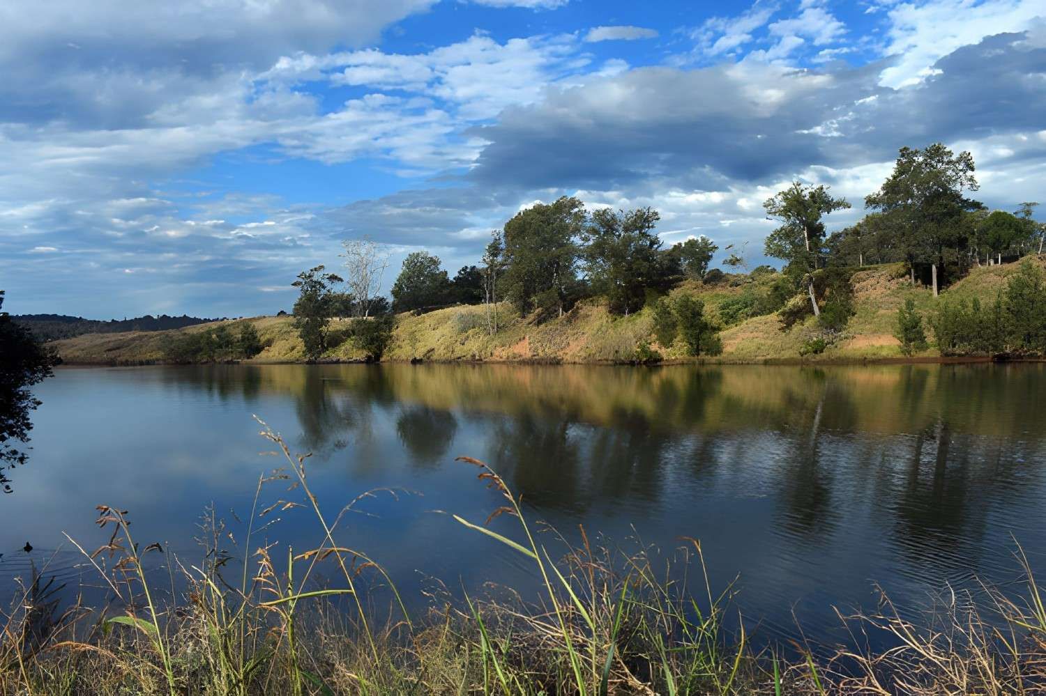 A Calm Lake Reflecting a Blue Sky with Clouds — Barry Brown Rural Contracting Service in Wingham, NSW