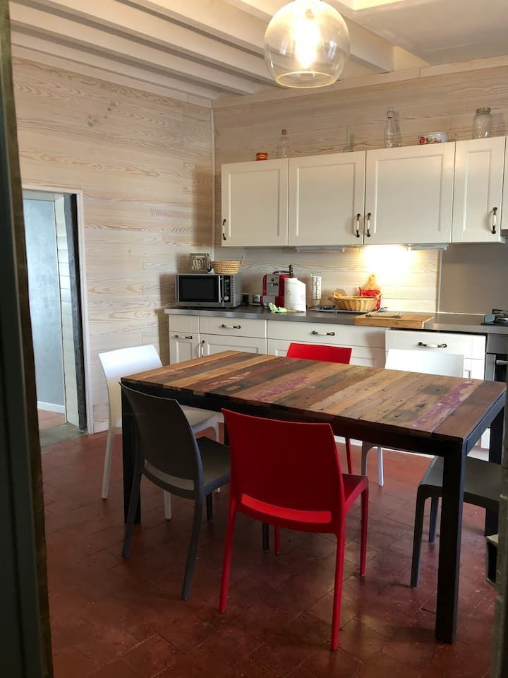 Cuisine avec une table en bois, des chaises rouges et noires, des placards blancs et une fenêtre lumineuse.