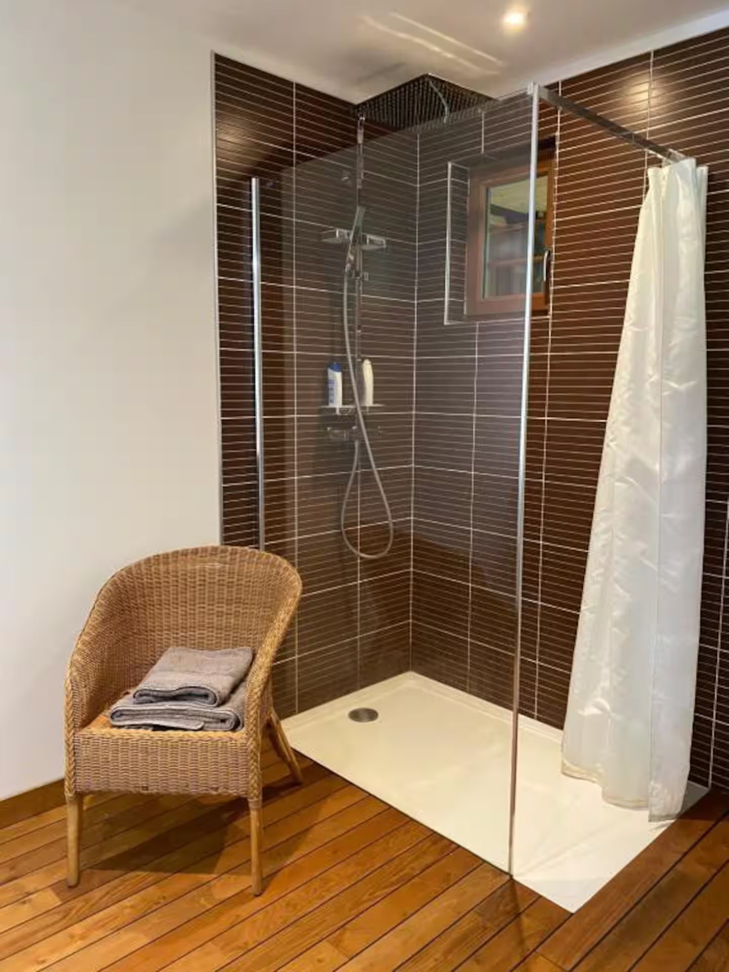 Une salle de bain avec douche à l'italienne et un fauteuil en osier.