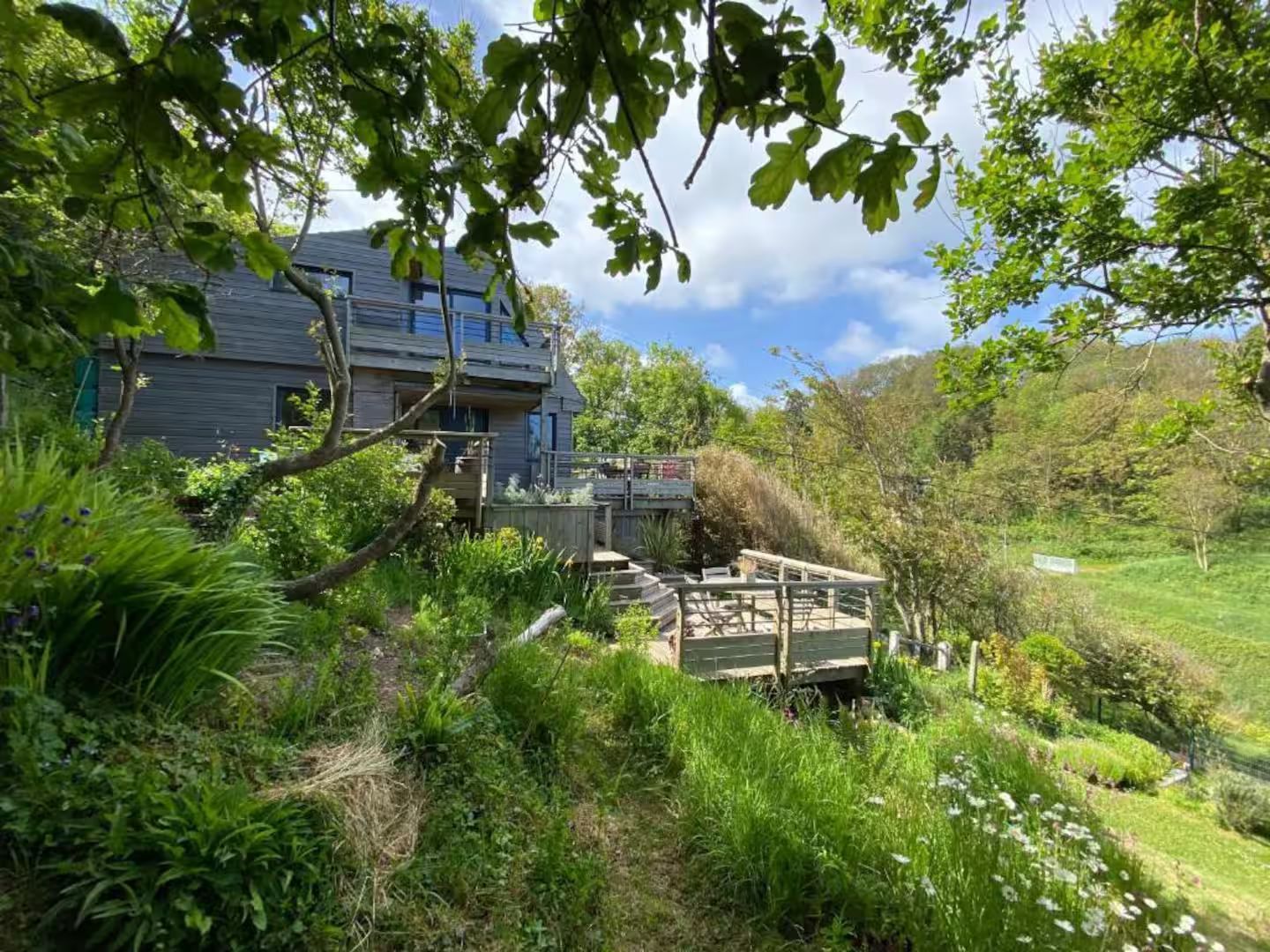 Une maison est située au sommet d'une colline entourée d'arbres et d'herbe.
