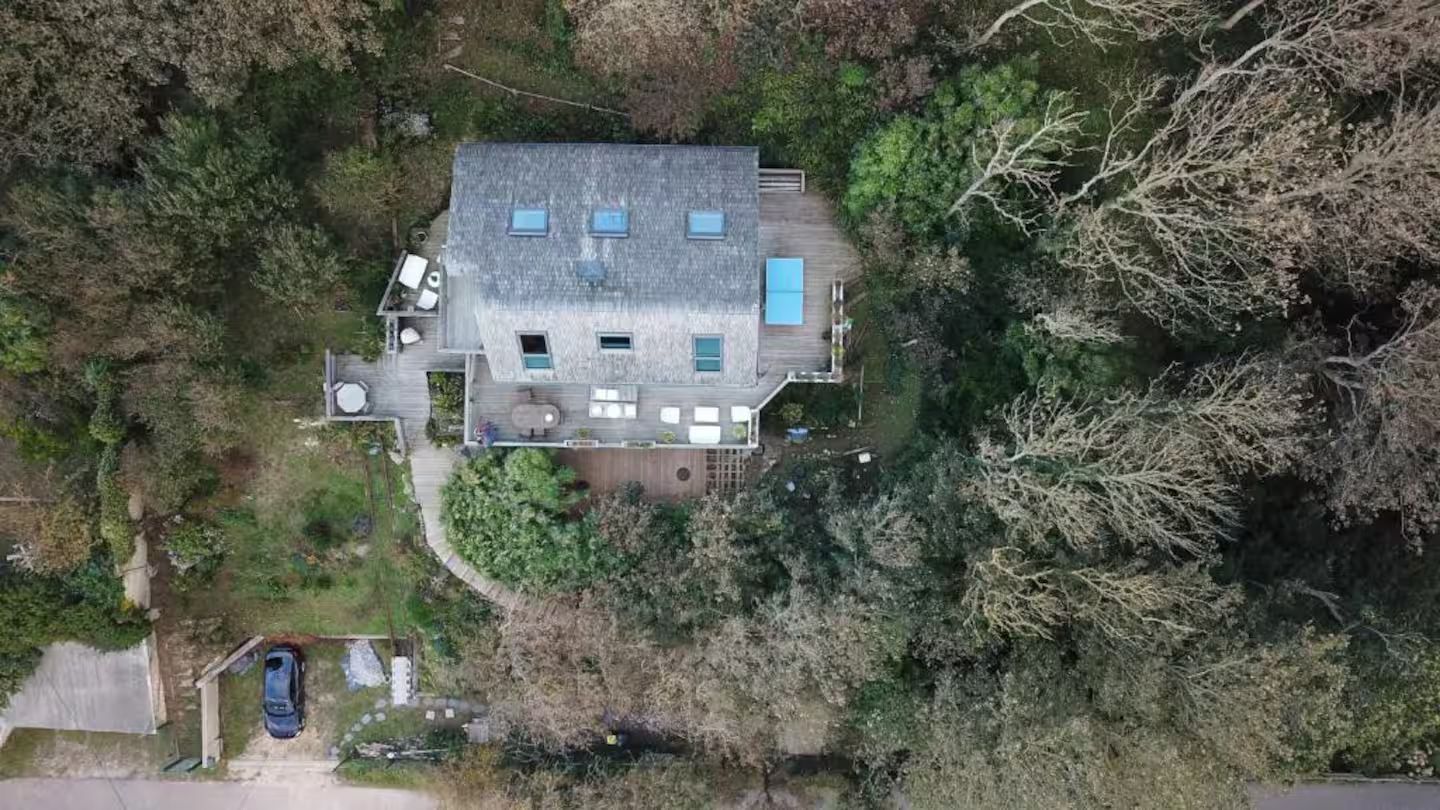Une vue aérienne d'une maison au milieu d'une forêt entourée d'arbres.