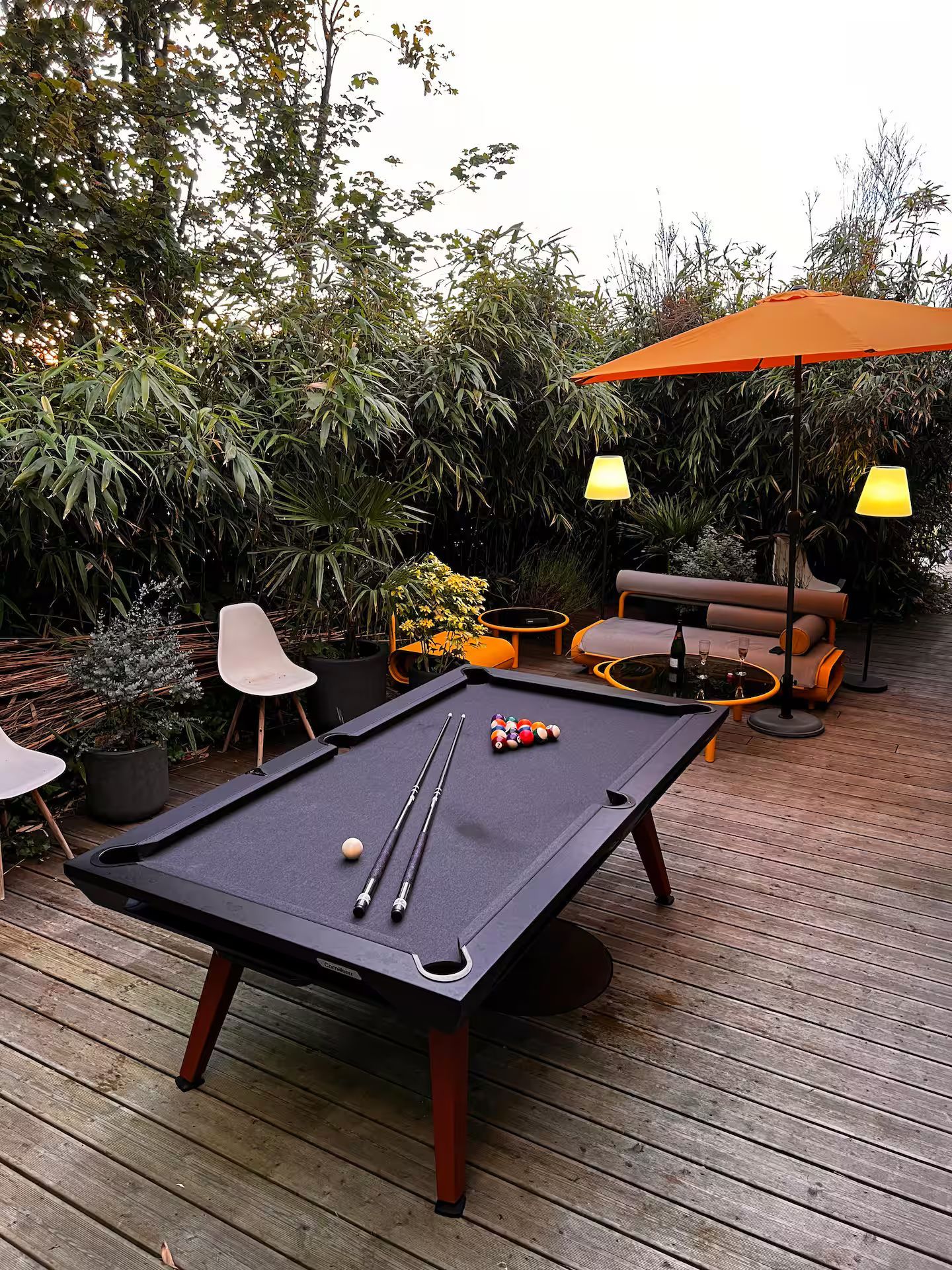 Une table de billard est posée sur une terrasse en bois sous un parasol orange