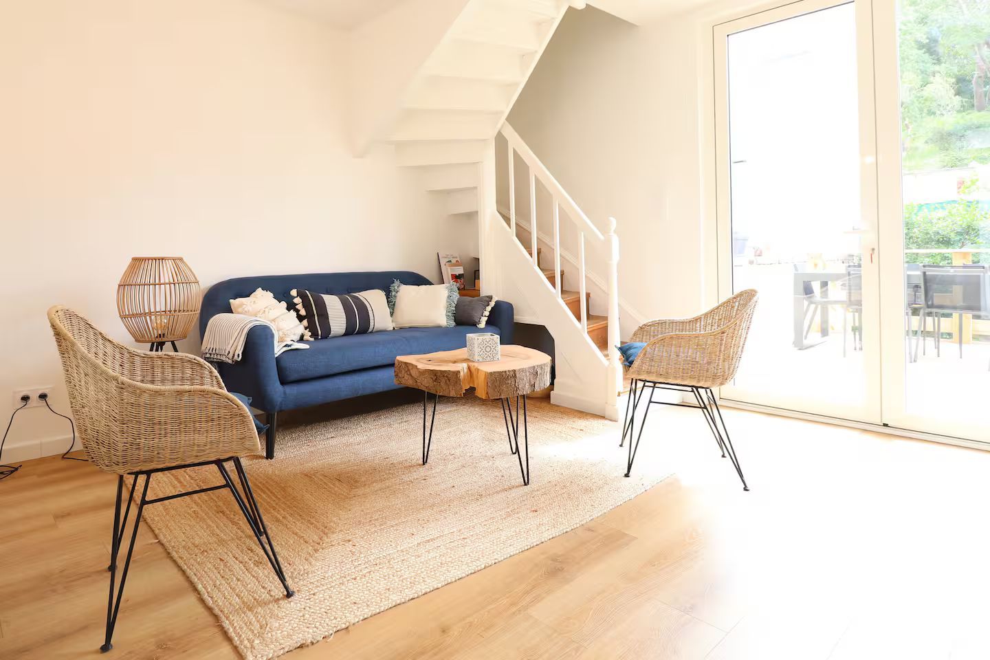 Un salon avec un canapé bleu, deux chaises, une table basse et des escaliers.