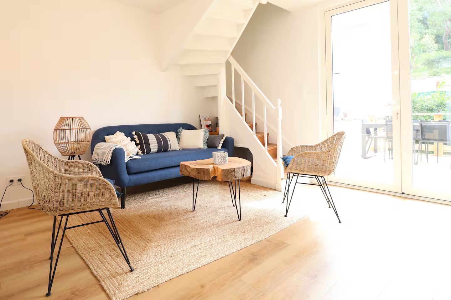 Un salon avec un canapé bleu, deux chaises, une table basse et des escaliers.