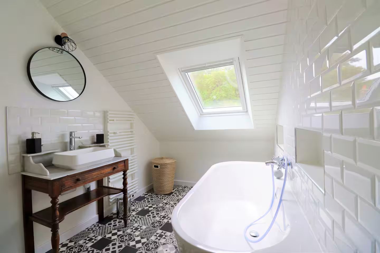 Une salle de bain avec baignoire, lavabo, miroir et puits de lumière.