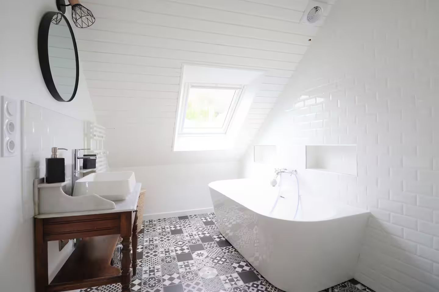 Une salle de bain avec baignoire, lavabo, miroir et puits de lumière.
