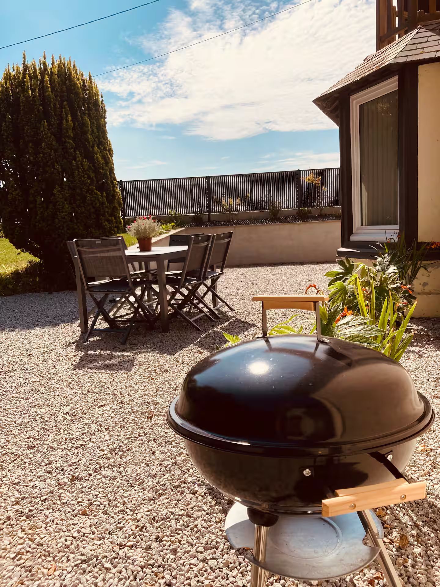 Un barbecue est posé sur le gravier devant une maison.