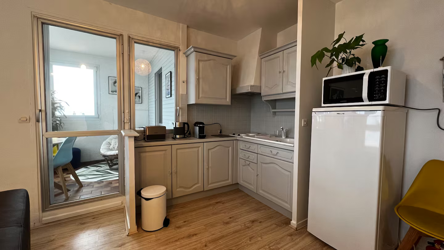 Une cuisine avec un réfrigérateur, un micro-ondes et une poubelle.