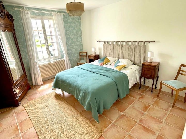 Chambre avec lit, meubles anciens, sol en terre cuite et tapis en jute.