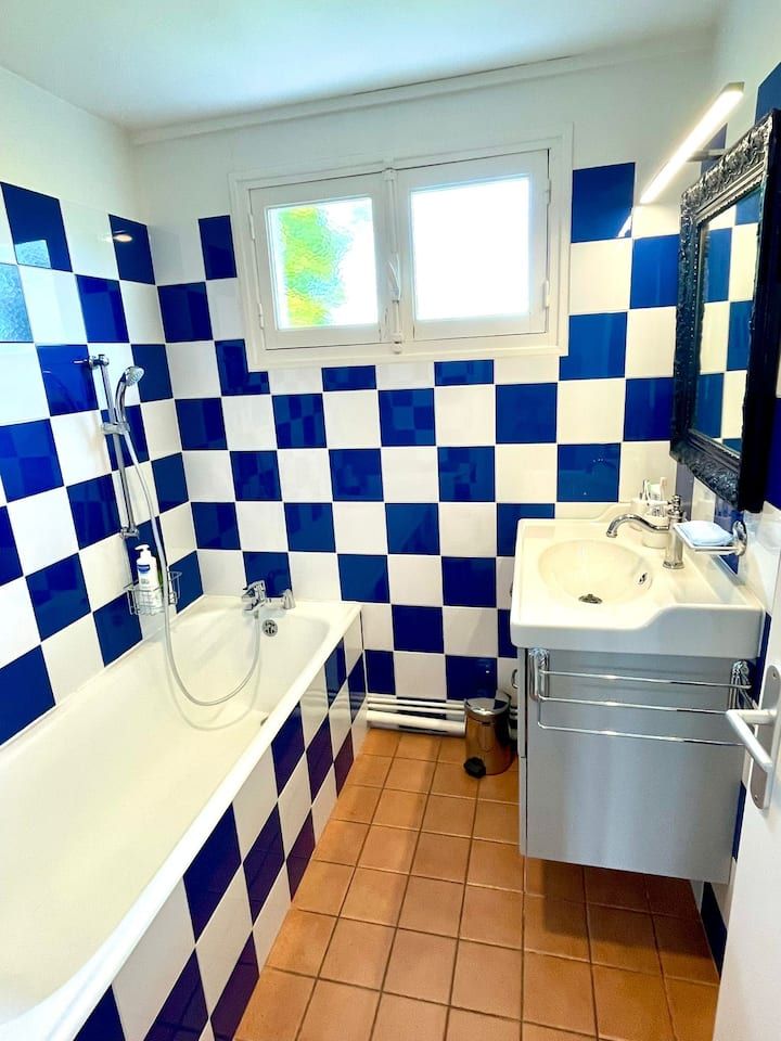 Salle de bains avec murs carrelés de carreaux à damier bleus et blancs, baignoire blanche et petite fenêtre.