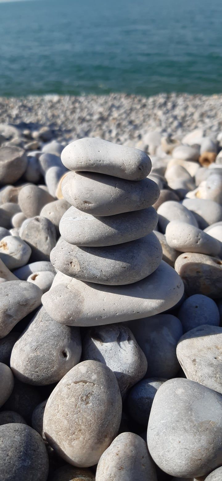 Un amas de rochers gris en équilibre sur une plage de galets, avec l'océan en arrière-plan.