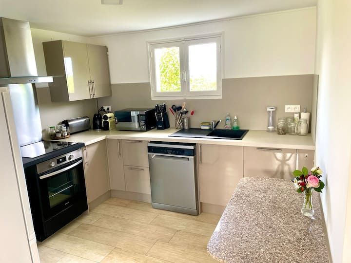 Petite cuisine avec des placards beiges, des appareils électroménagers en acier inoxydable et une table ornée d'un arrangement floral.