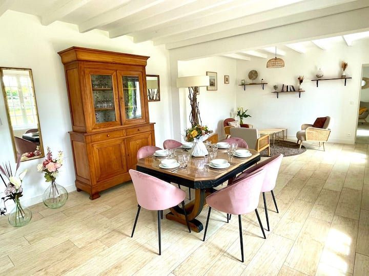 Salle à manger avec buffet en bois, table dressée avec chaises roses et coin salon.