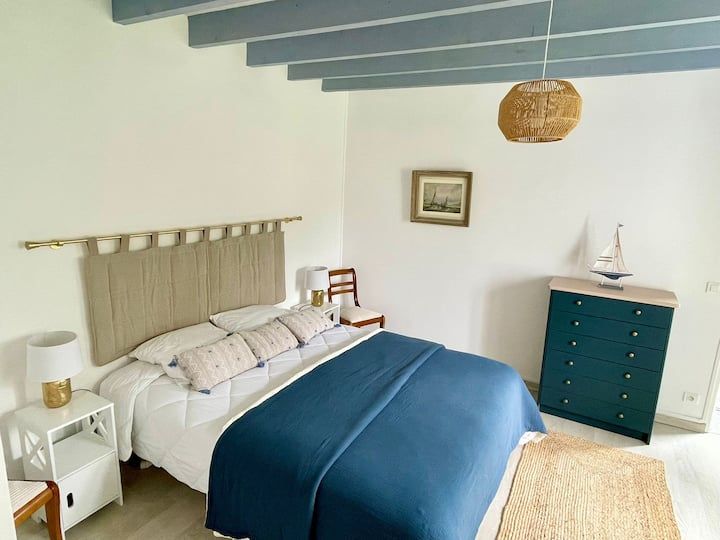 Chambre avec des touches de bleu : lit, commode et poutres apparentes au plafond, avec un abat-jour et un tapis tissés.