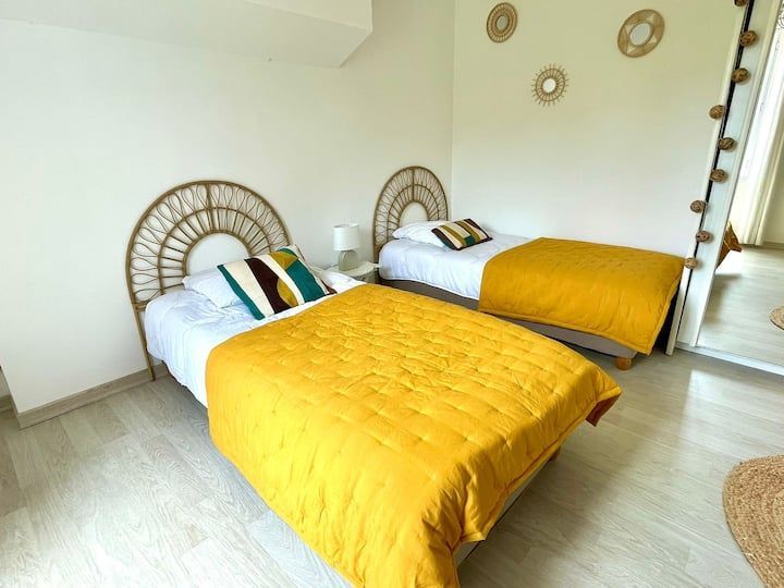 Deux lits jumeaux dans une chambre lumineuse avec des draps jaunes et des têtes de lit en osier.