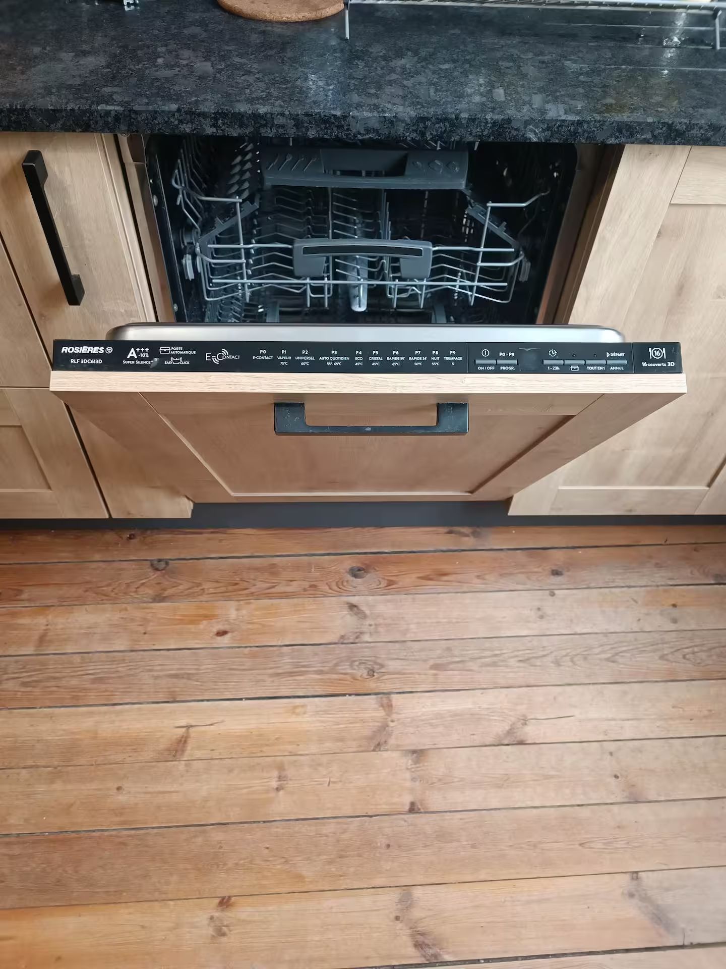 Un lave-vaisselle est ouvert dans une cuisine avec un plancher en bois.