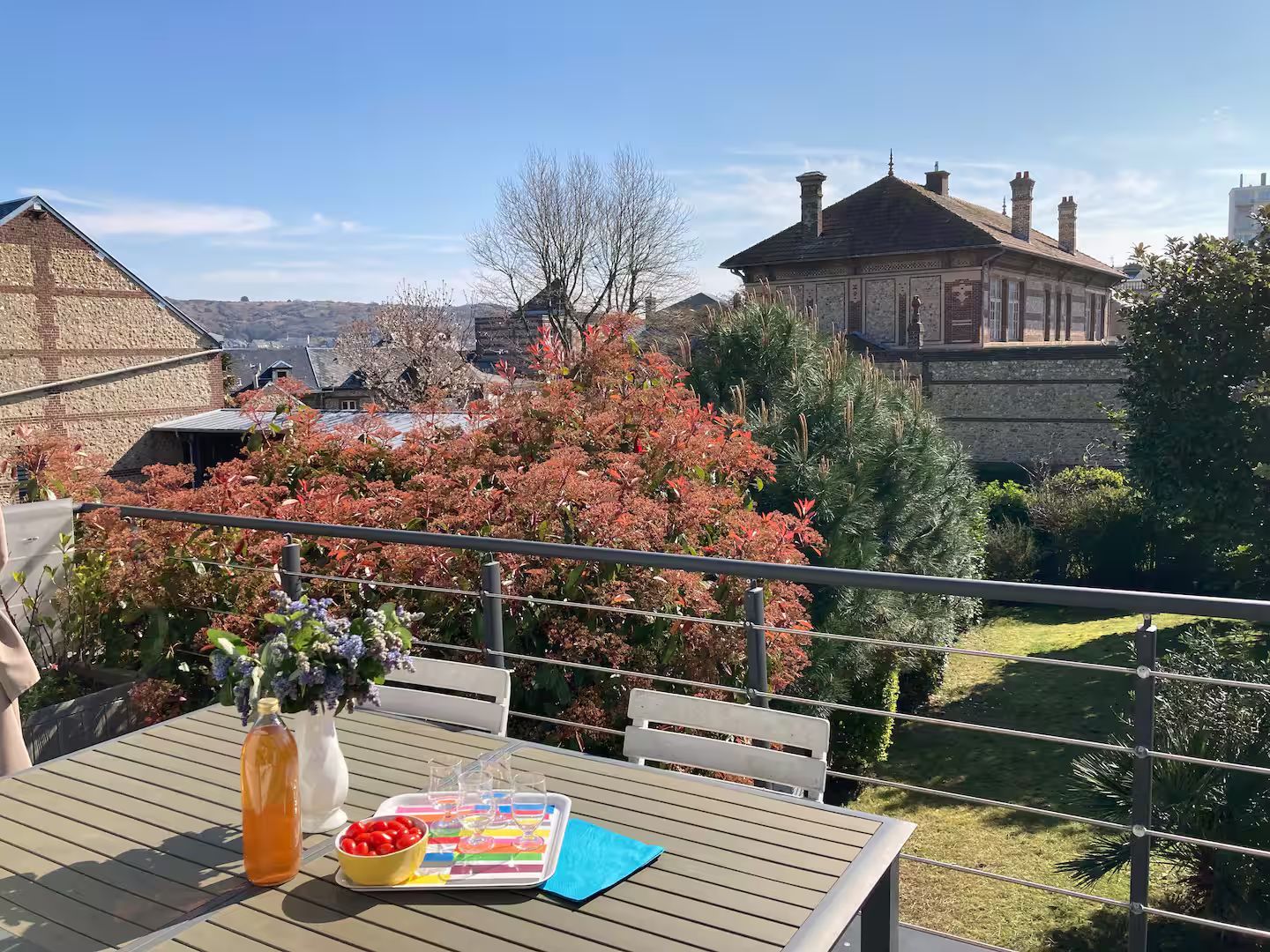 Une table avec une bouteille de jus d'orange dessus se trouve sur un balcon donnant sur un jardin.