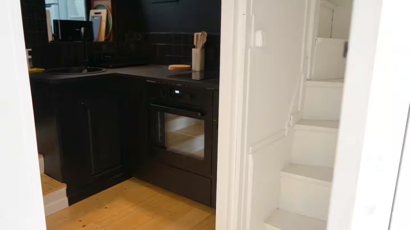 Une cuisine avec une cuisinière noire et des escaliers qui y mènent.