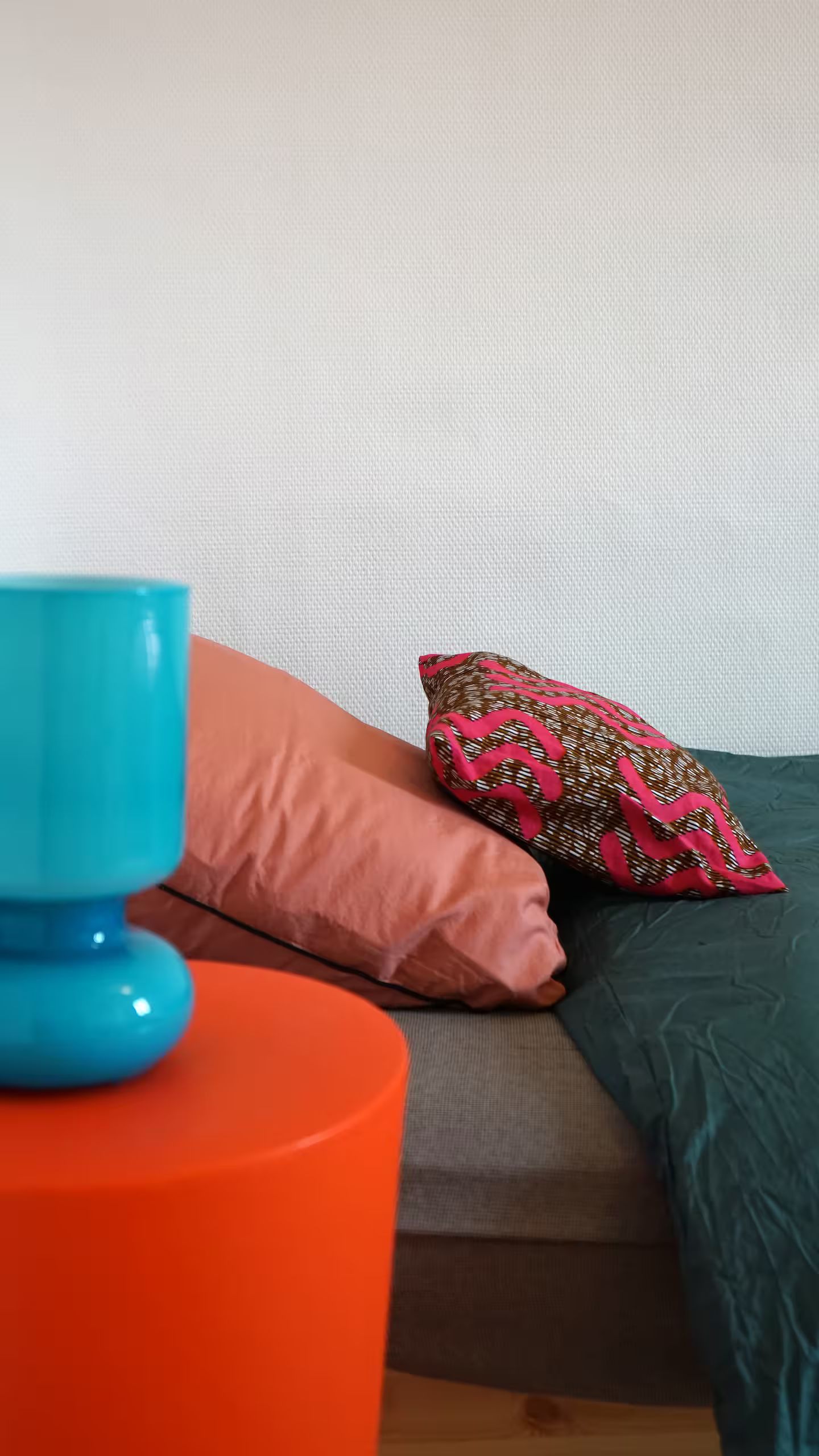 Un vase bleu est posé sur une table orange à côté d'un lit.