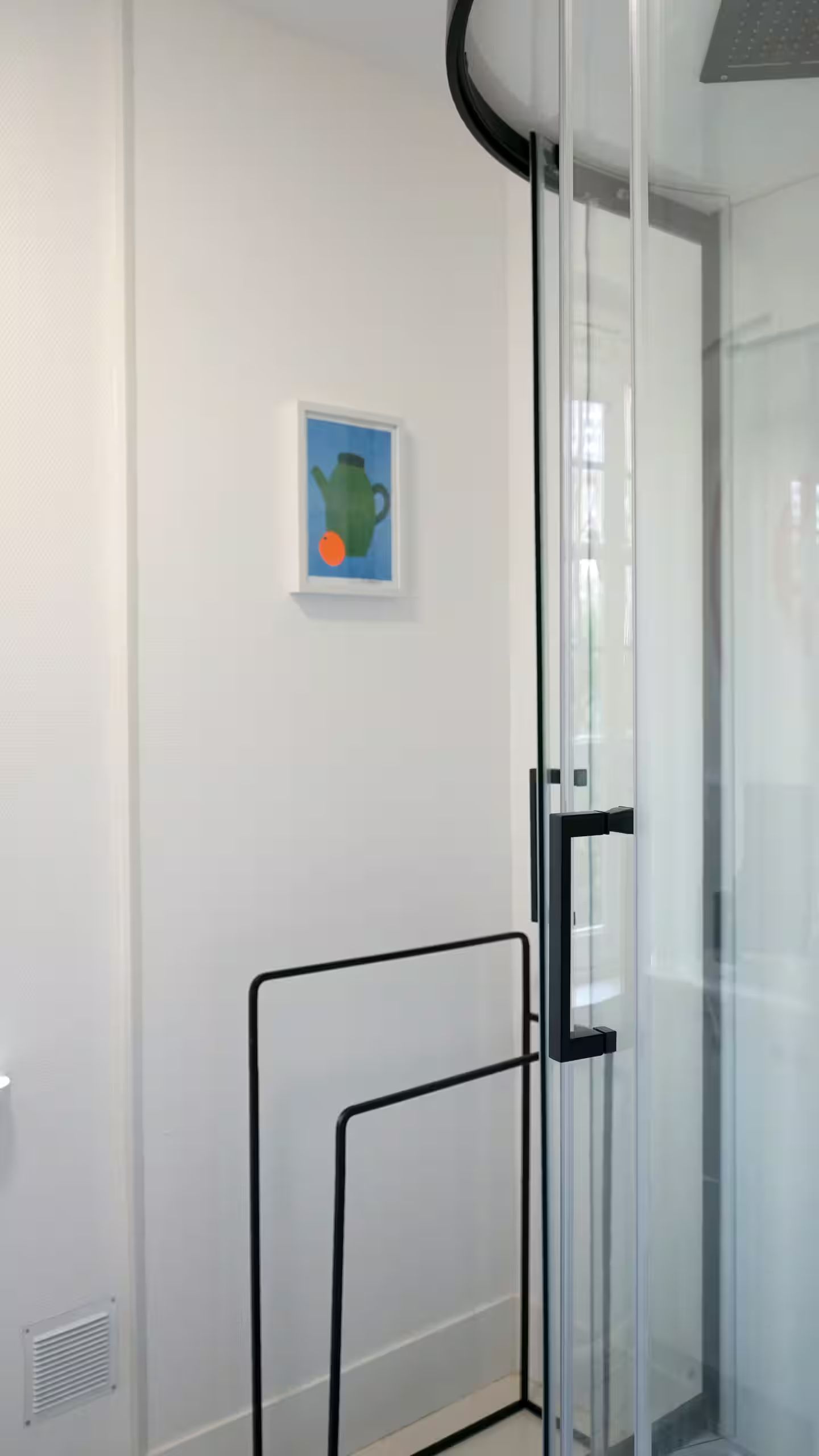 Une image d'une théière est accrochée au mur au-dessus d'un porte-serviettes dans une salle de bain.