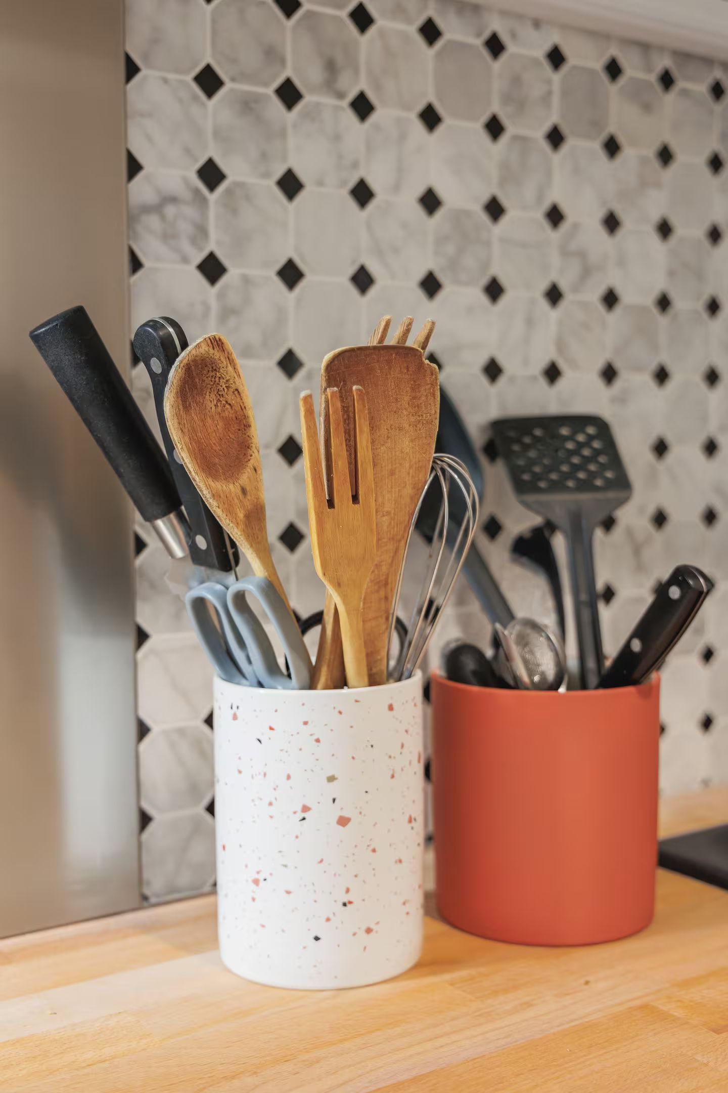 Deux porte-ustensiles remplis d'ustensiles et de couteaux sur un comptoir de cuisine.