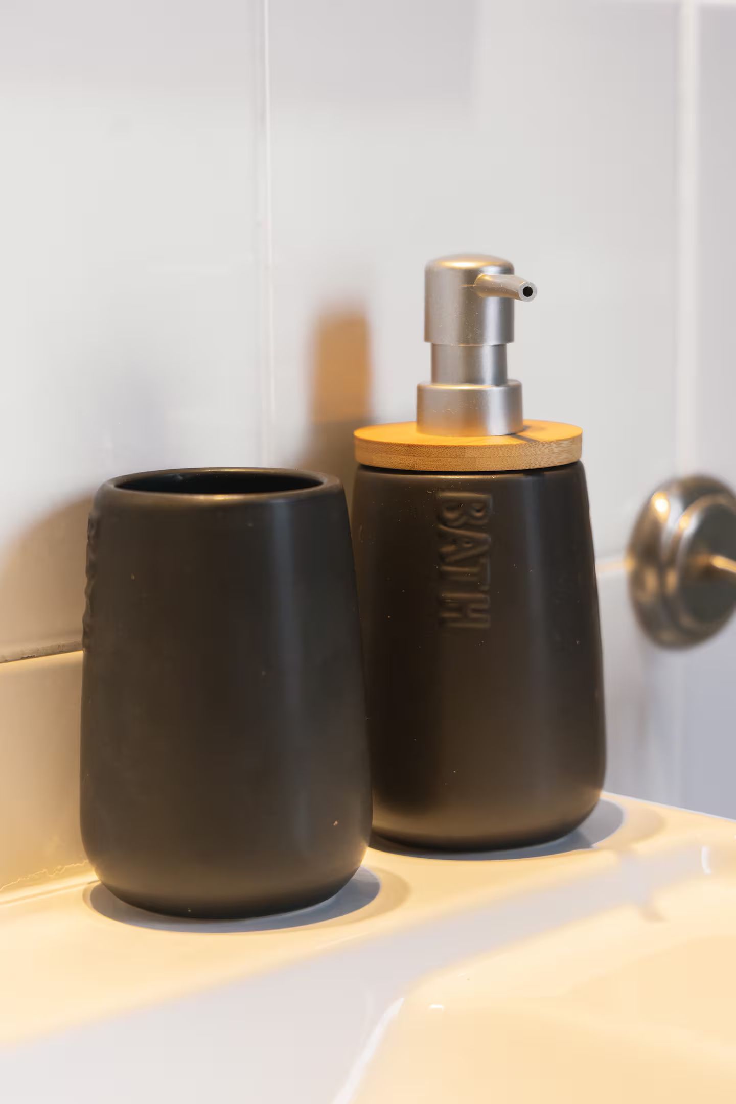 Un distributeur de savon noir et une tasse noire se trouvent sur un lavabo de salle de bain.