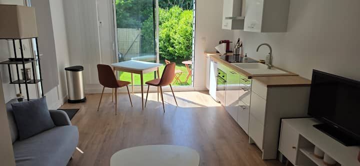 Salon moderne et lumineux avec canapé, télévision, table à manger et portes coulissantes donnant sur un jardin ensoleillé.