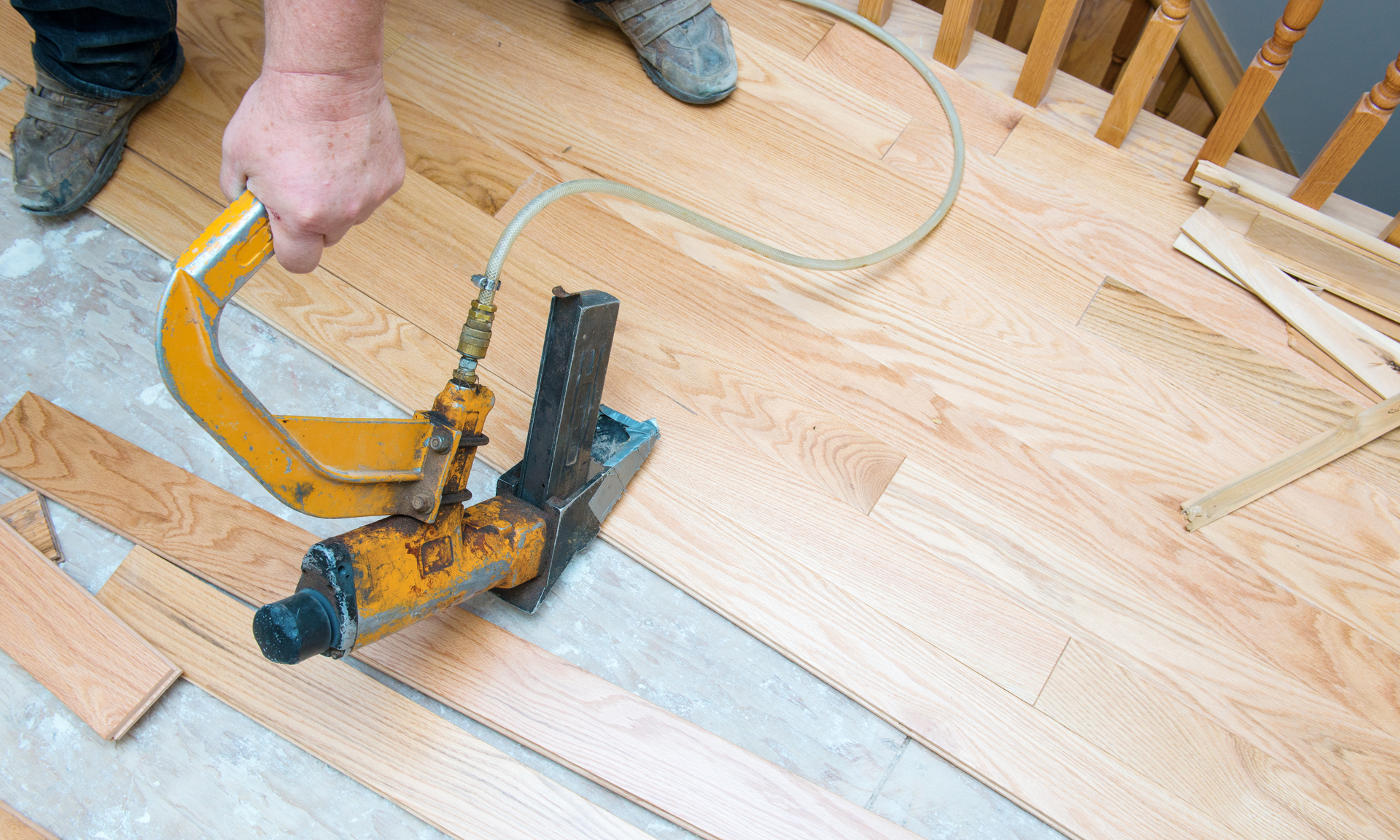 A photo of a flooring contractor installing hardwood flooring planks with a nail gun.
