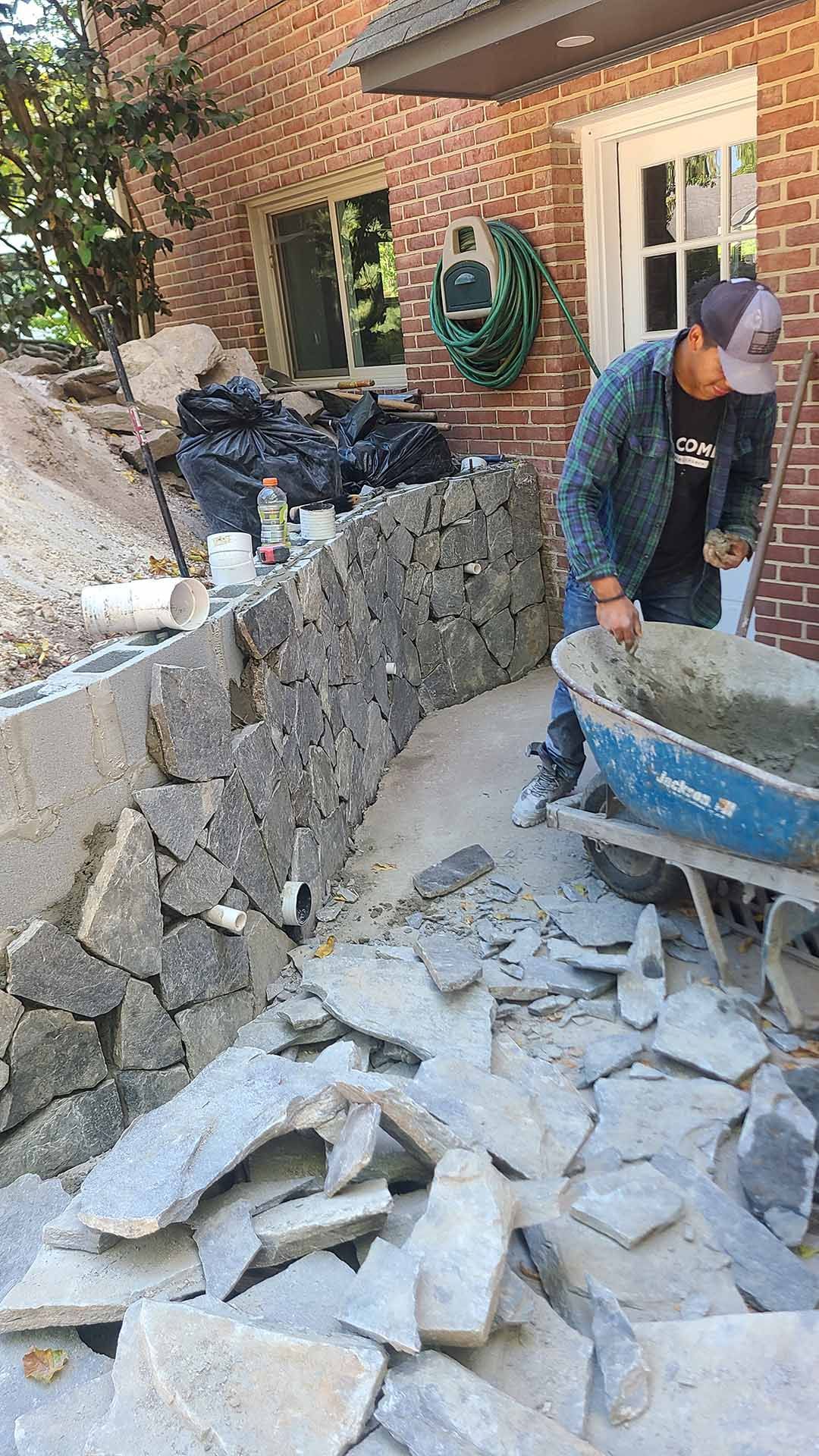 A man is mixing cement in a wheelbarrow in front of a brick building
