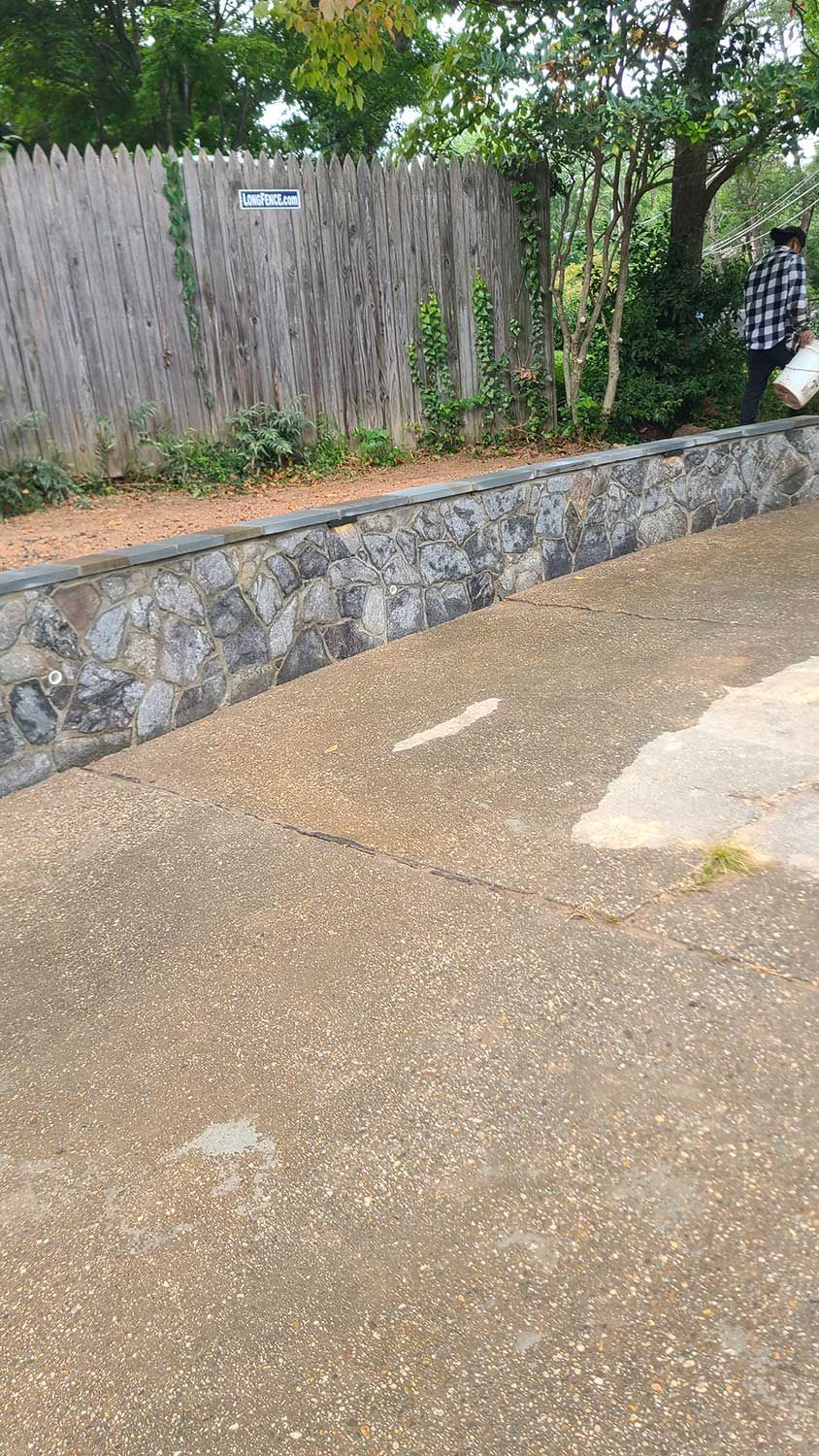 A person is walking down a sidewalk next to a stone wall