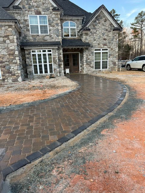 A large stone house with a brick driveway in front of it