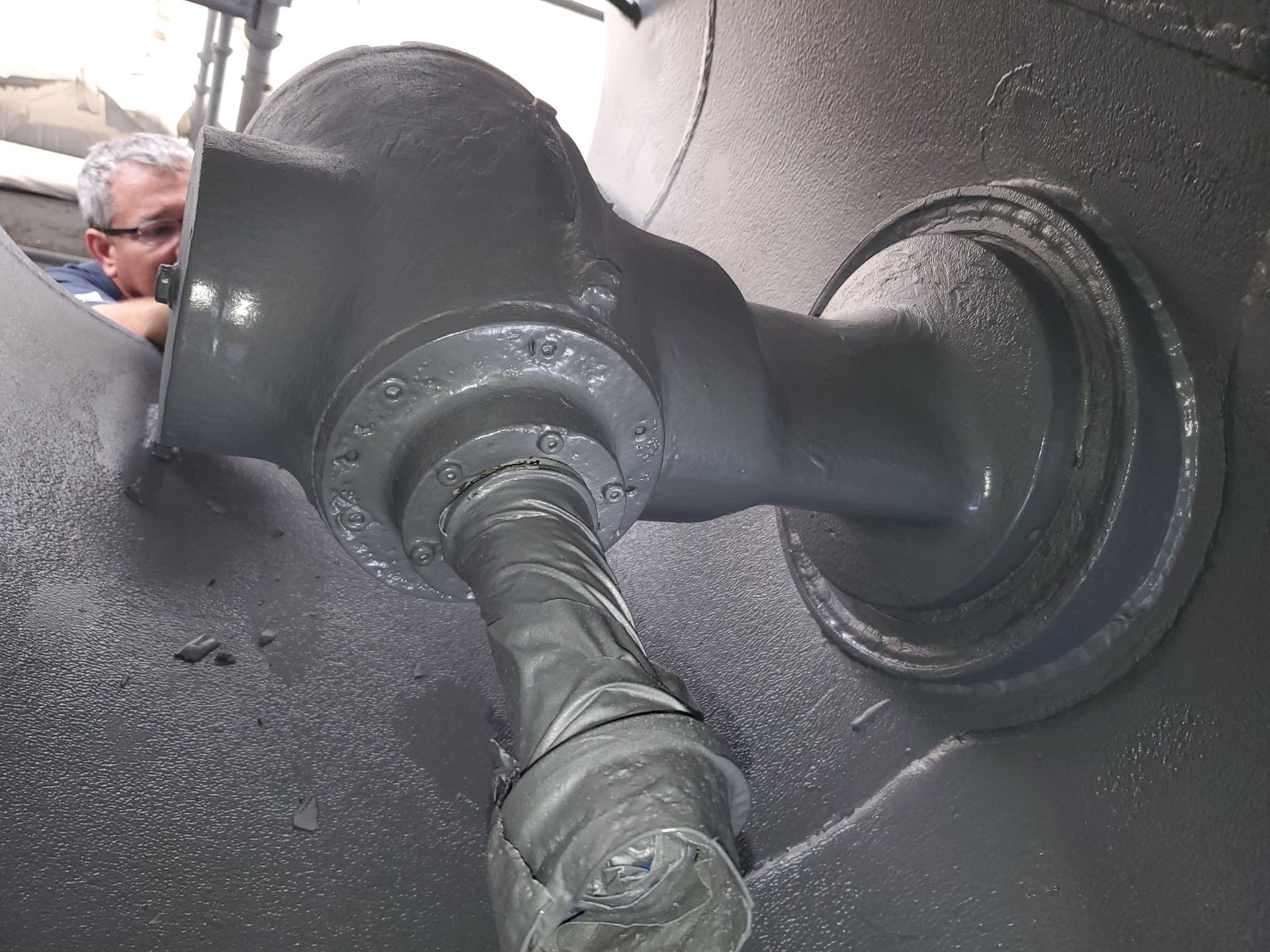 A man is looking at a pipe that is covered in gray paint