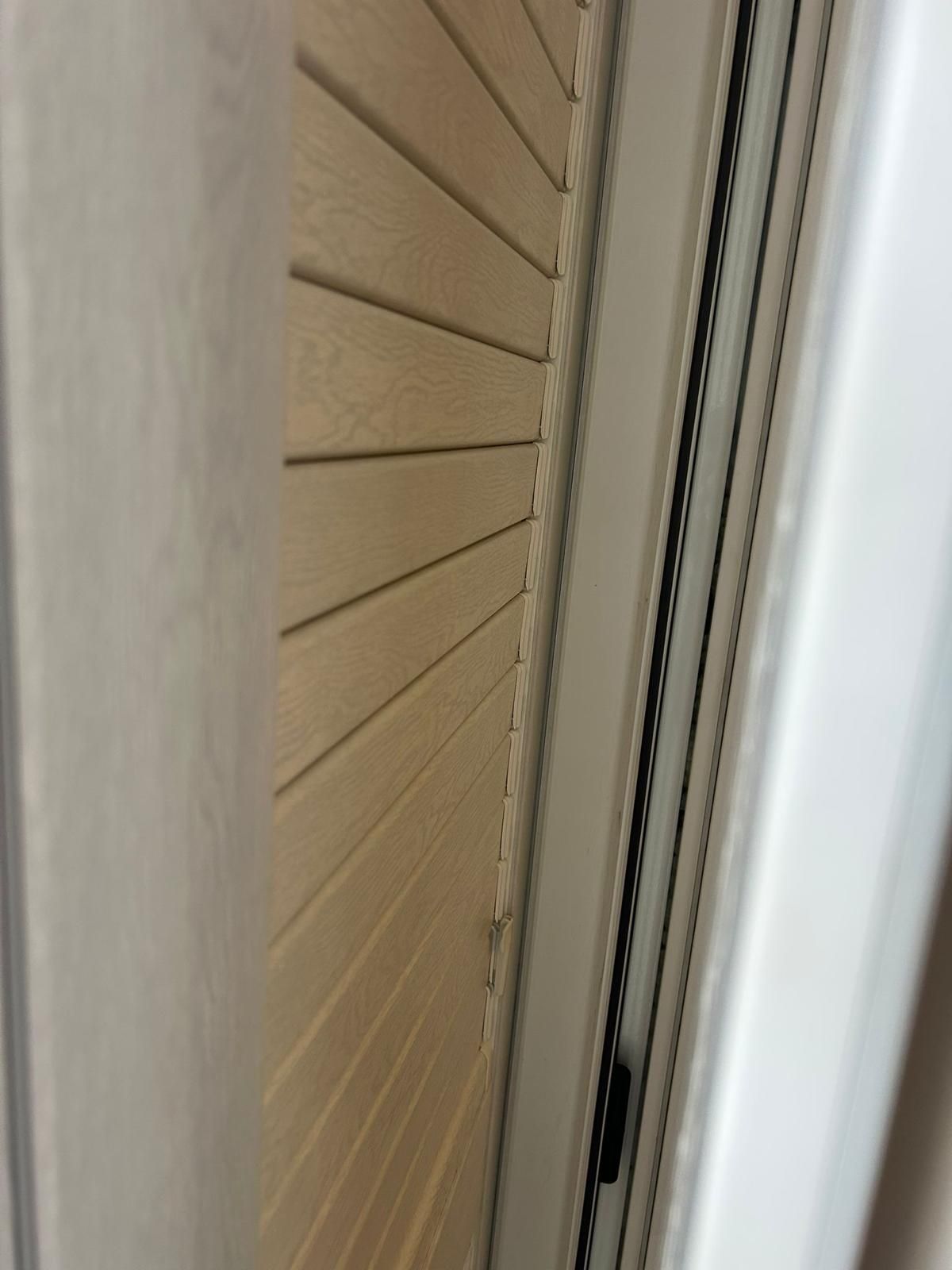 Persiane in legno beige inclinate contro il telaio bianco della finestra.