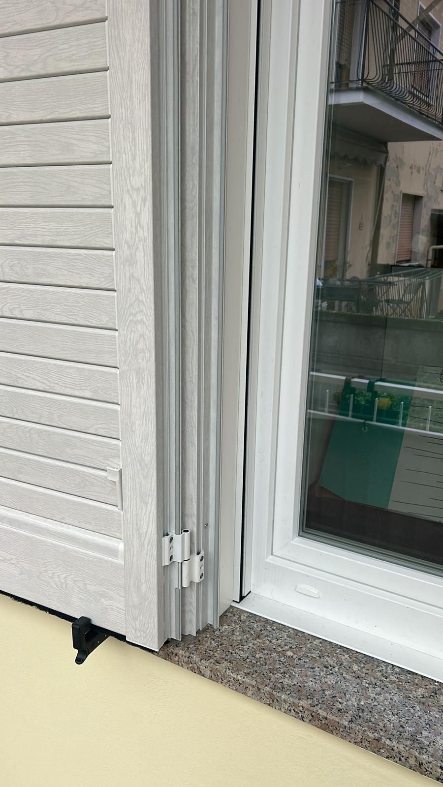 Persiana bianca e telaio della finestra di un edificio, davanzale in pietra, vista esterna con sfondo sfocato.