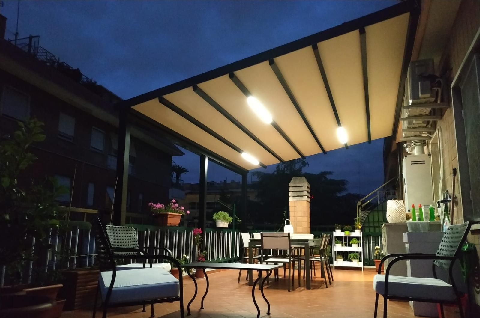 Un patio con tenda da sole retrattile al tramonto, con tavoli e sedie sistemati.