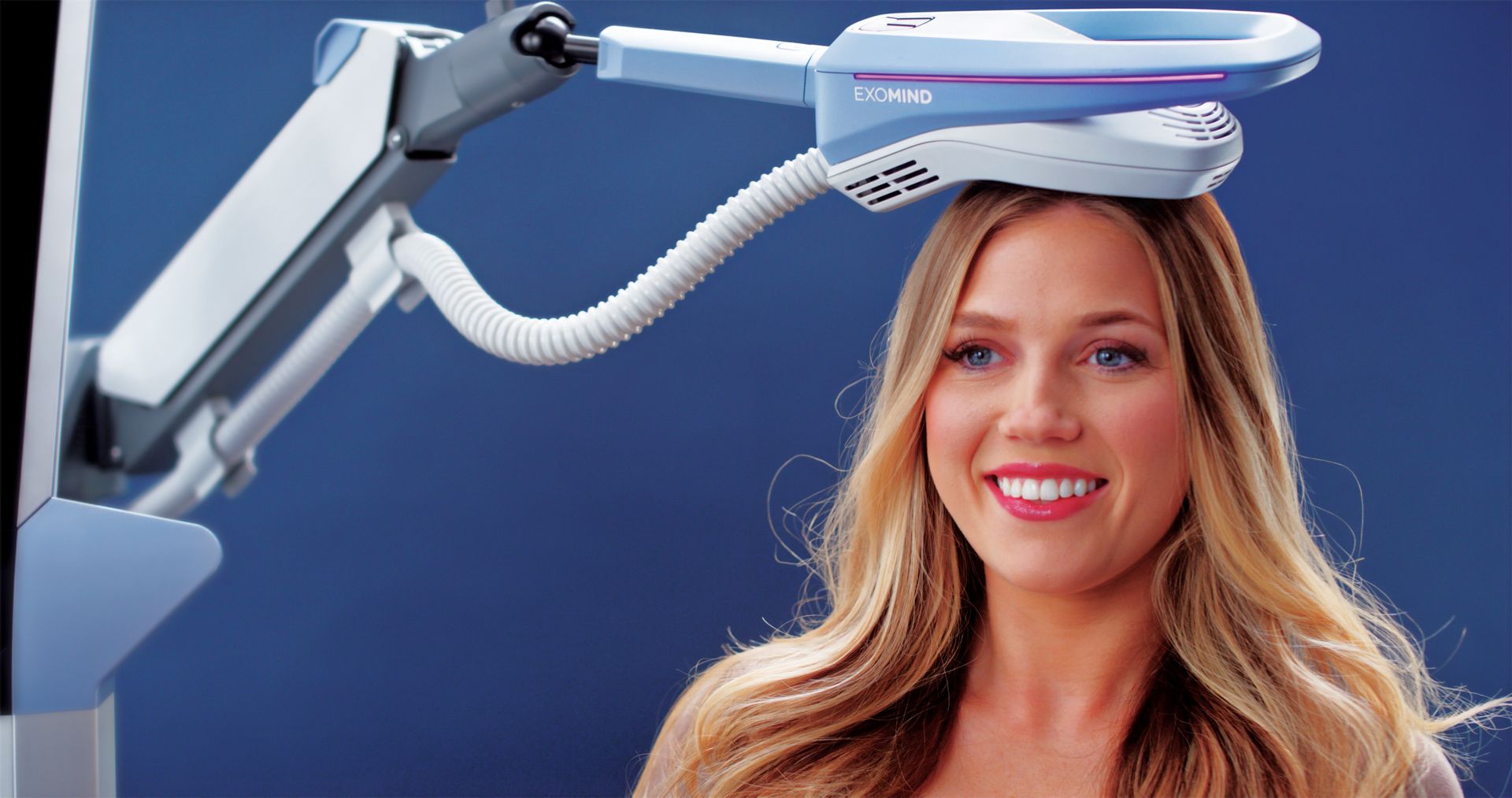 Woman undergoing TMS treatment; machine positioned over head, smiling.