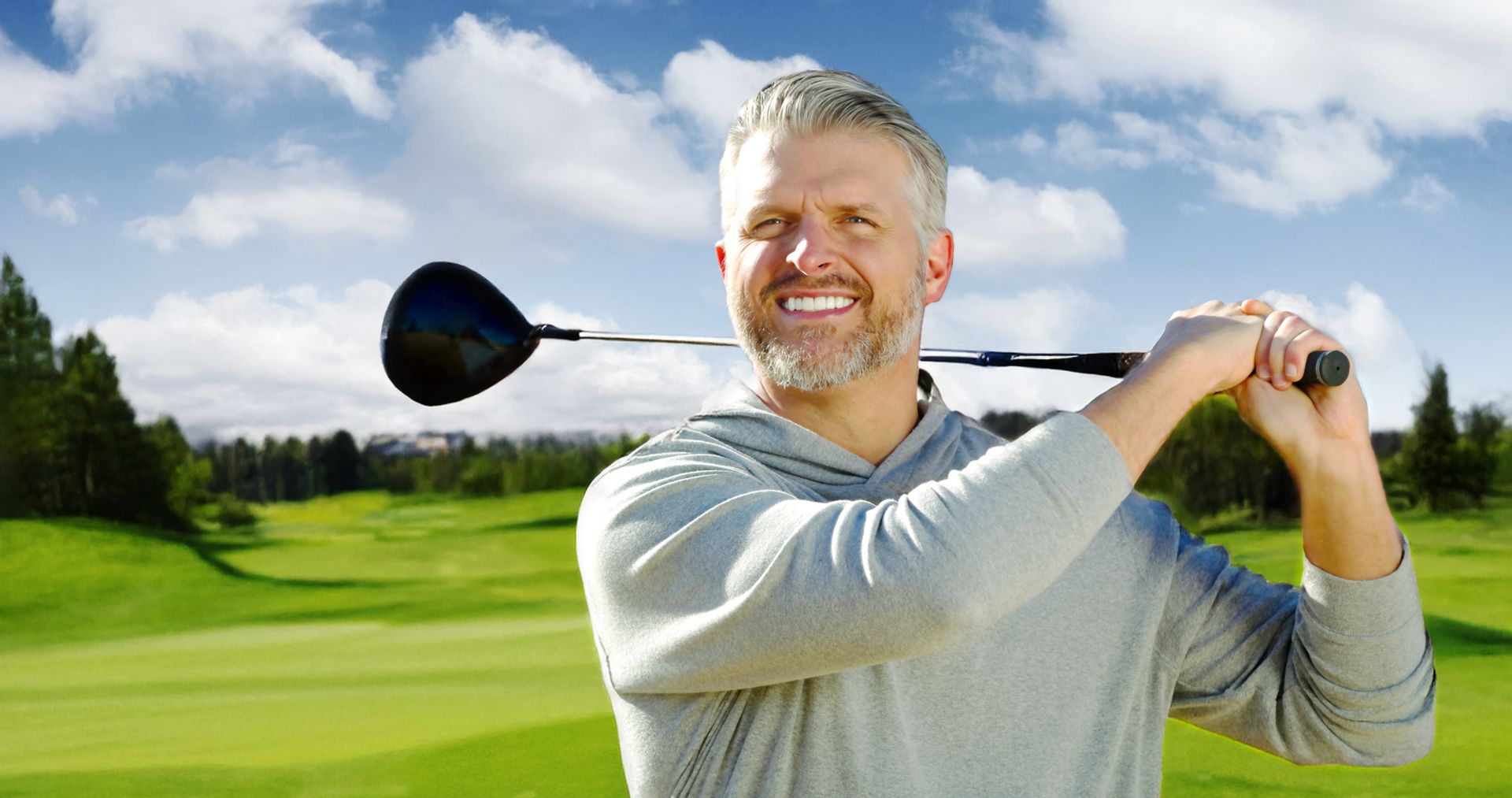 Man holding a golf club on a green course, smiling.