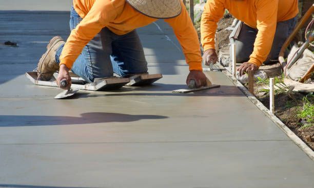 Local concrete contractors in orange uniforms, finishing work on the freshly poured concrete.