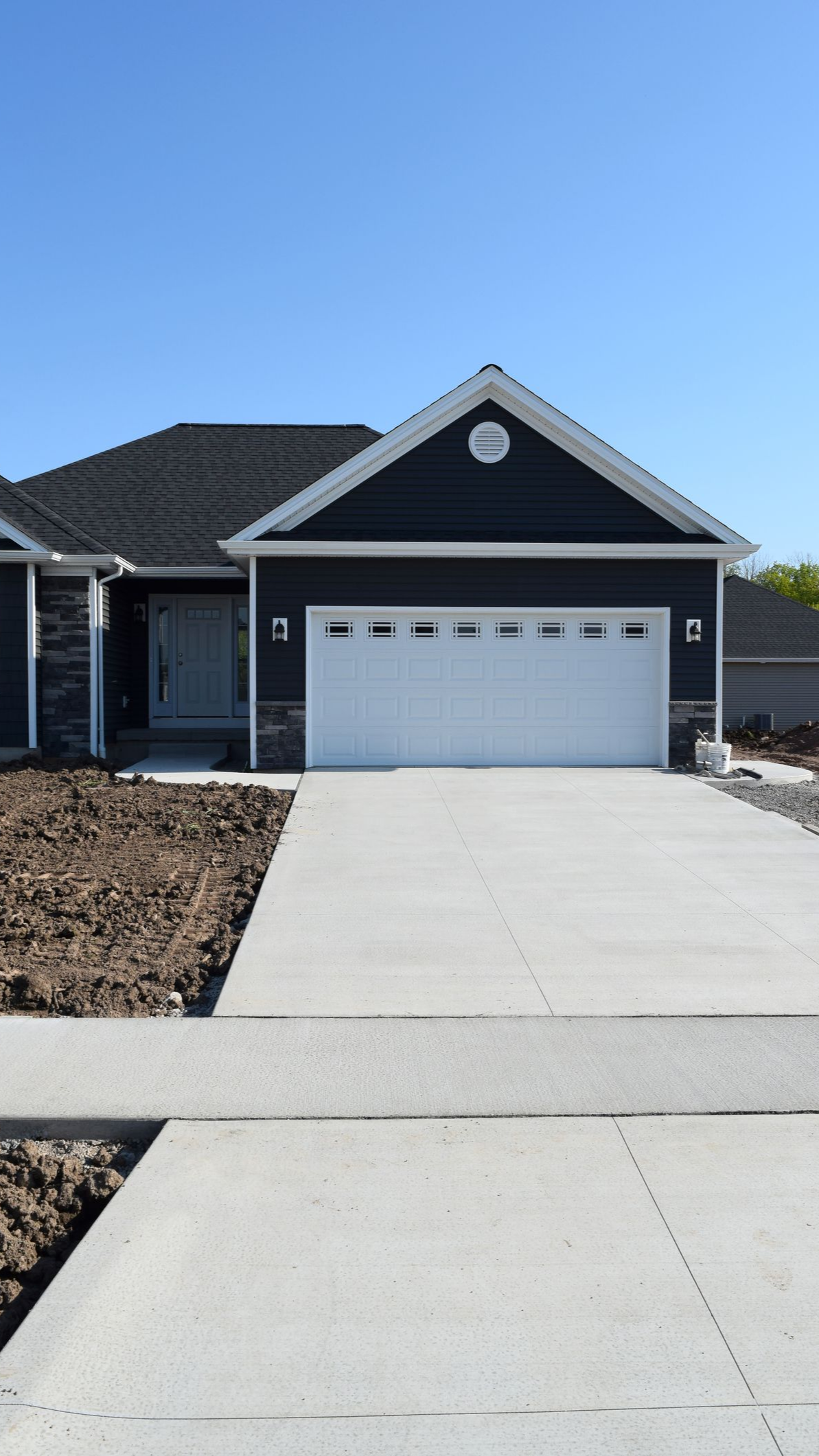Blue-sided house with white garage door and concrete driveway on a sunny day.