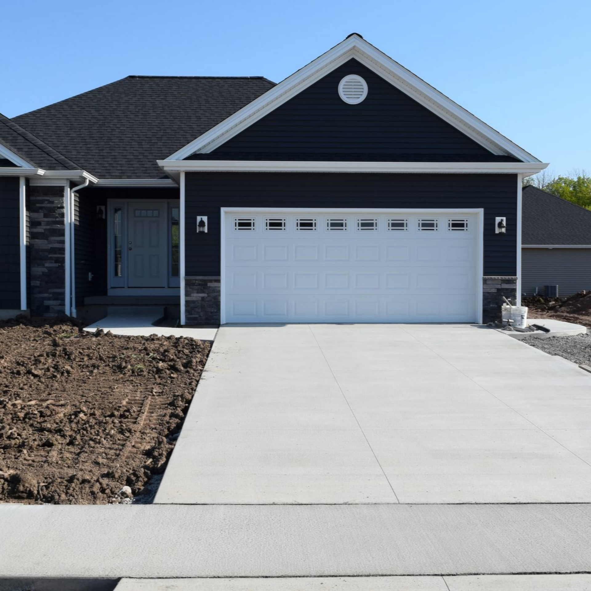 Blue-sided house with white garage door and concrete driveway on a sunny day.
